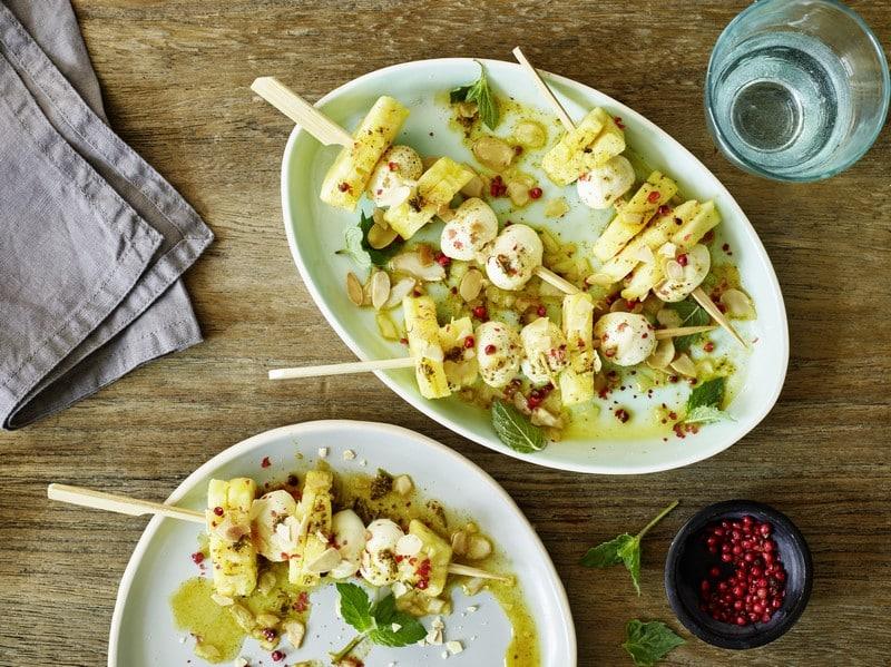 Brochettes apéritif chic d'ananas frais et mozzarella nappées de sirop orange romarin Fuchs, baies roses Fuchs, amandes effilées torréfiées et menthe fraîche