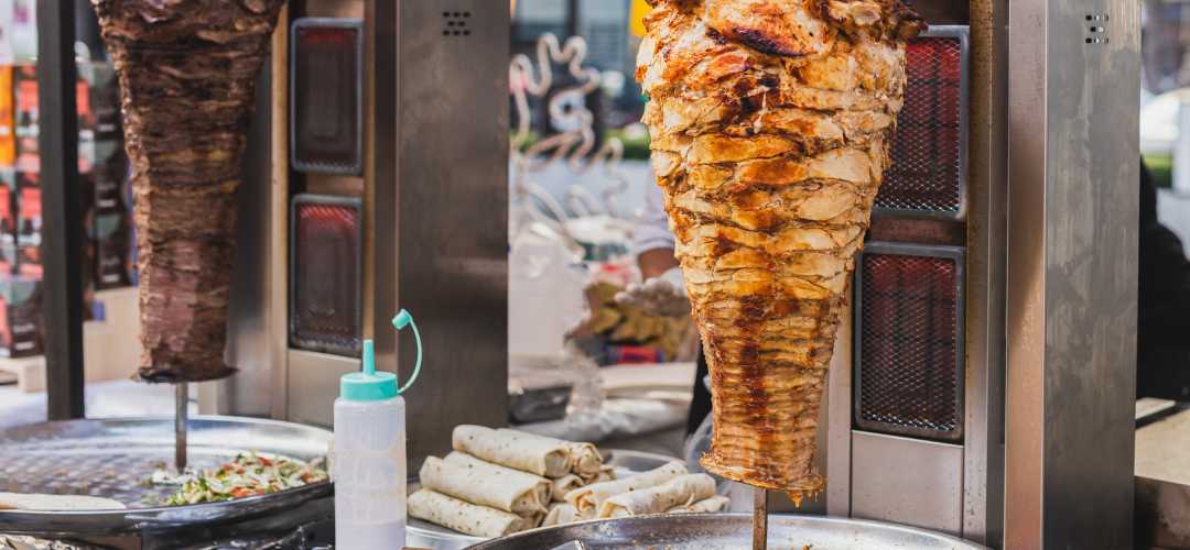 Kebab traditionnel turc en cours de cuisson sur broche verticale tournante avec pain pita, crudités et sauce blanche