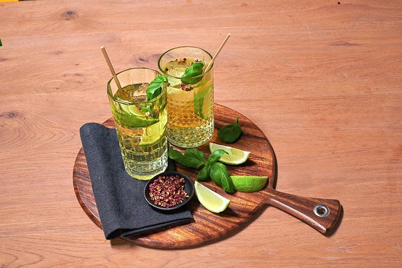 Verre de cocktail Gin Tonic givré avec des glaçons, quartiers de citron vert, feuilles de basilic et grains de poivre de Sichuan Fuchs